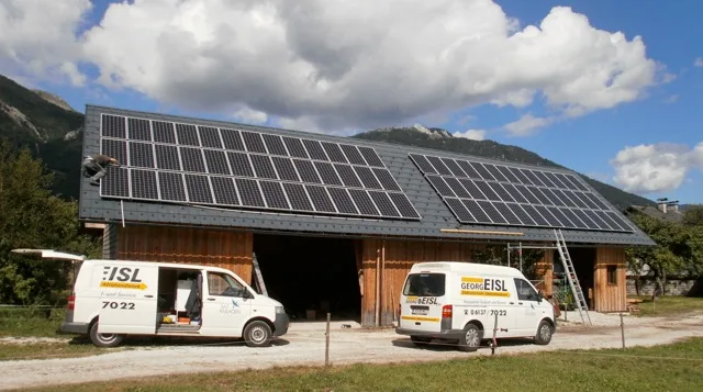 Gebäude mit großer Photovoltaikanlage, davor zwei Firmenfahrzeuge von Elektro Eisl
