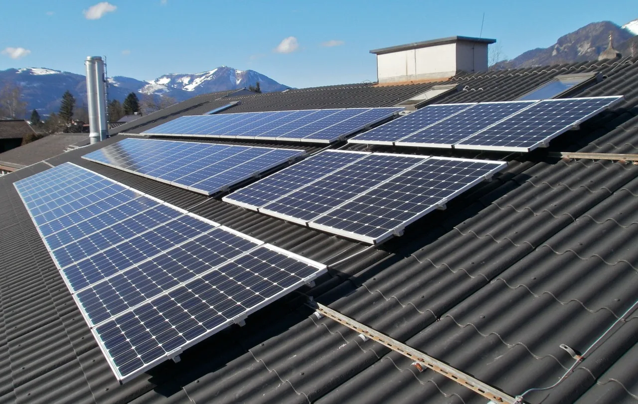 Photovoltaikmodule werden auf einem dunklen Dach montiert, im Hintergrund Berge